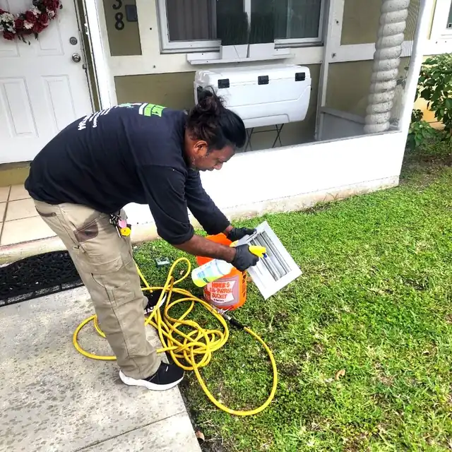 Technician cleaning AC vent covers outside the home